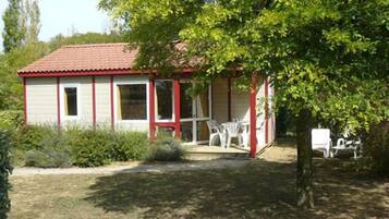 A small, single-story building with a red-tiled roof and a porch with white plastic chairs.