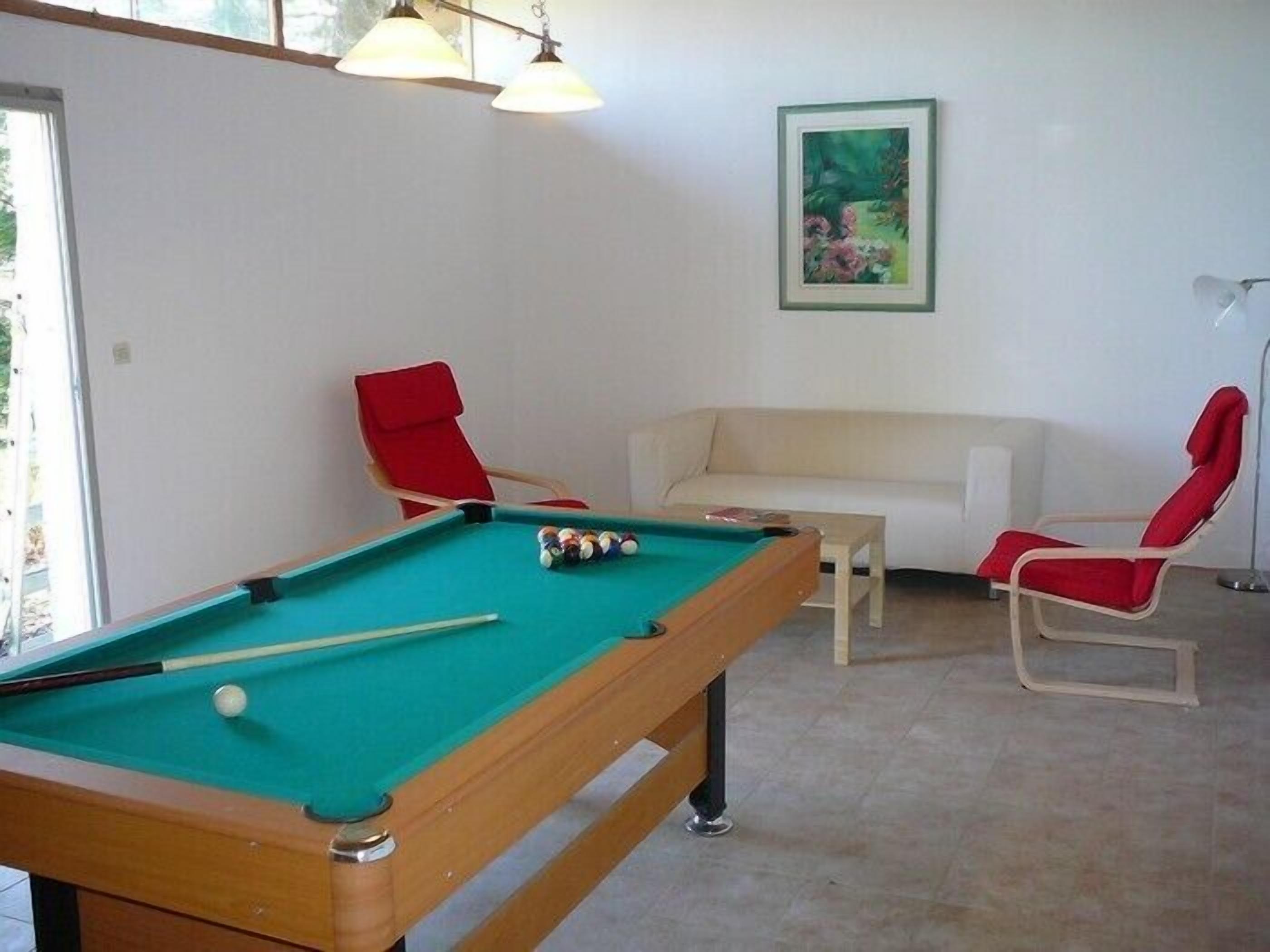 A pool table with balls, a red chair, a white sofa, and a framed picture on the wall.