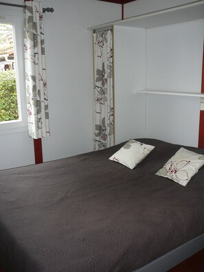 Cozy bed with a floral-patterned headboard, set against a white wall with a window and shelf.