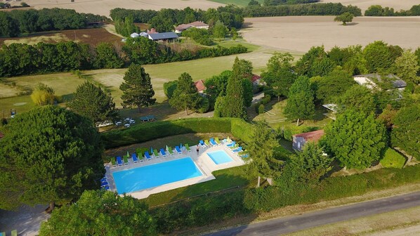 Surrounded by lush greenery and a well-maintained lawn, this property offers a serene setting with a large swimming pool and various buildings.