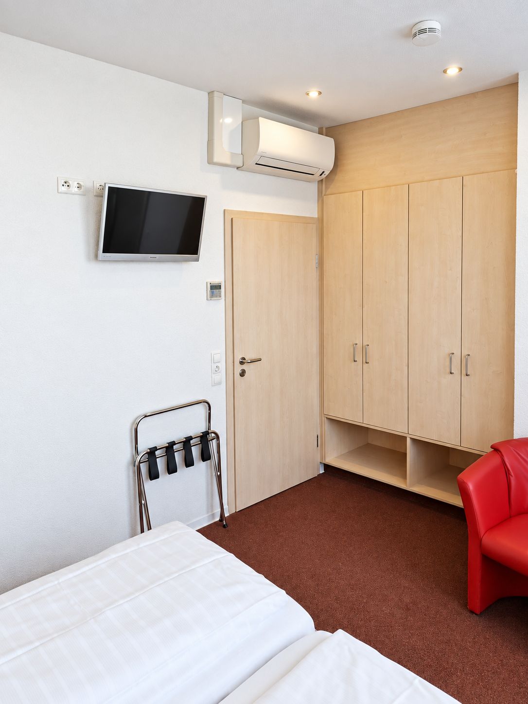 Habitación de hotel con cama, televisión, armario y una silla roja.