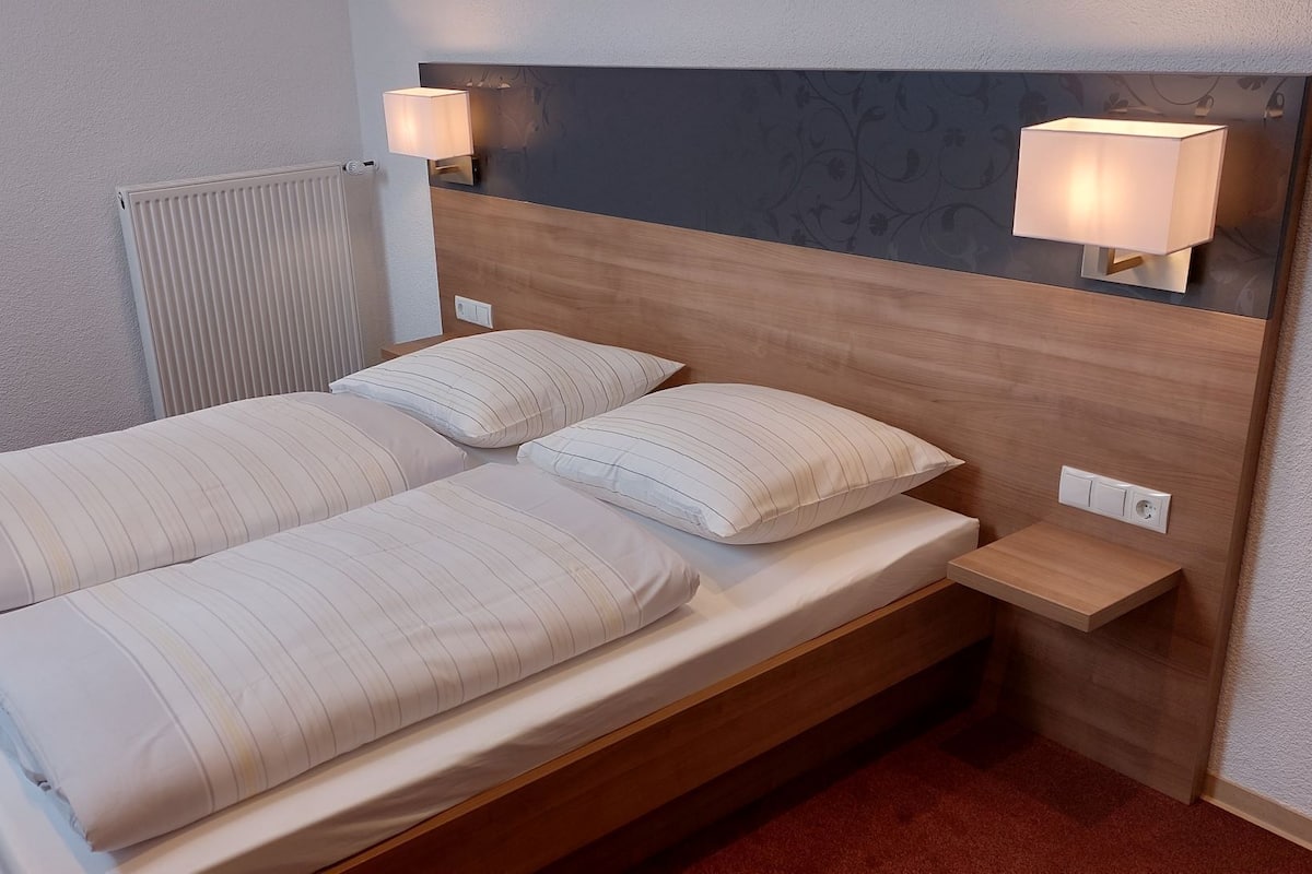 A double bed with striped bedding, a wooden headboard, two bedside lamps, and a small wooden nightstand with a power outlet.