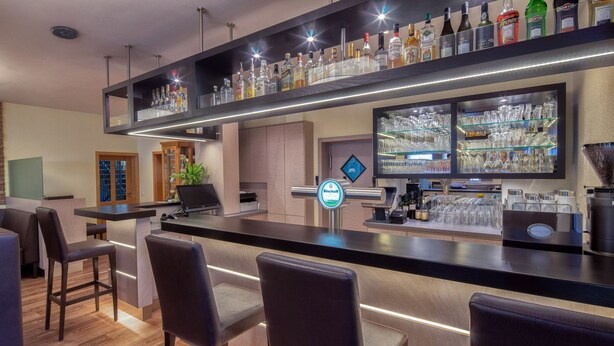 A modern bar area with a counter, bar stools, and shelves stocked with bottles and glasses. - HRC Pfeffermühle (Landstuhl)