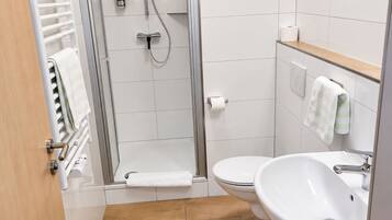 Un baño moderno con ducha envuelta en vidrio, un lavamanos blanco y un inodoro.