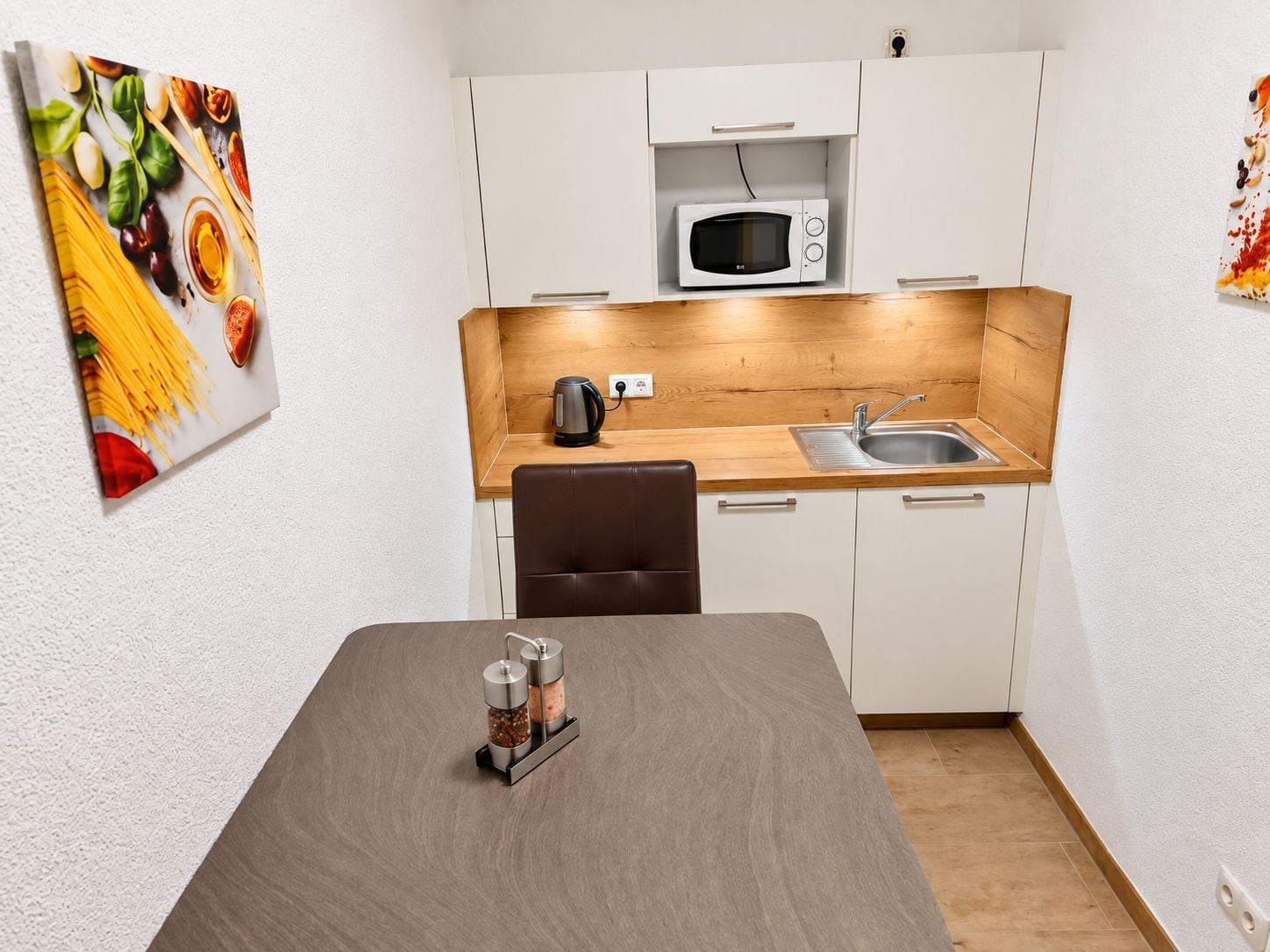 A compact kitchen with a microwave, kettle, and a wooden countertop.