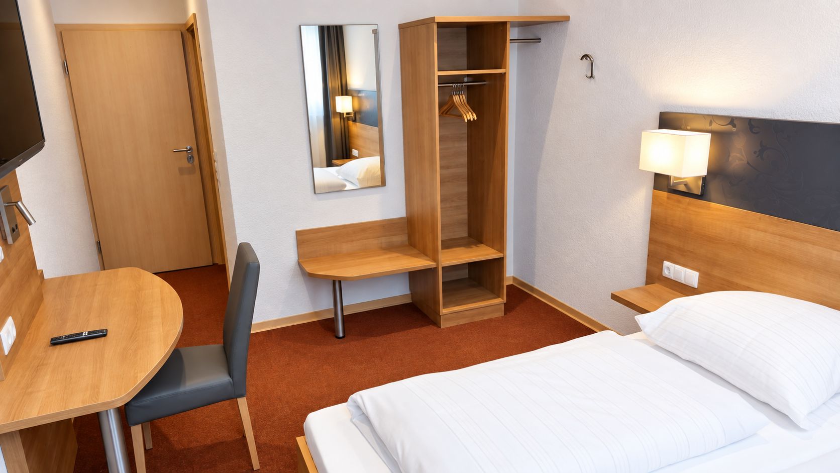 Een hotelkamer met een bed, een bureau, een stoel, een kledingkast, een spiegel en een bedlamp.