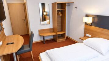 Een hotelkamer met een bed, een bureau, een stoel, een kledingkast, een spiegel en een bedlamp.