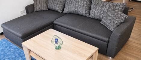 Ein modulares Sofa mit gemusterten Kissen, ein Couchtisch aus Holz mit einer Kerze und ein blauer Teppich mit Muster.
