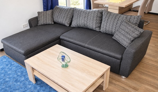 Un sofá modular con cojines estampados, una mesa de centro de madera con una vela y una alfombra azul estampada.