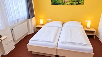 A hotel room with a double bed, two bedside tables with lamps, a radiator, a window with curtains, and a forest-themed wall art.