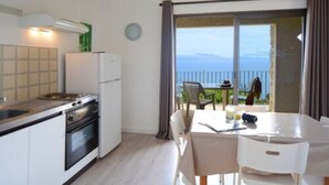 A kitchen with a stove, refrigerator, and a dining area with a table and chairs. - Résidence Roc e Mare (Cargese)