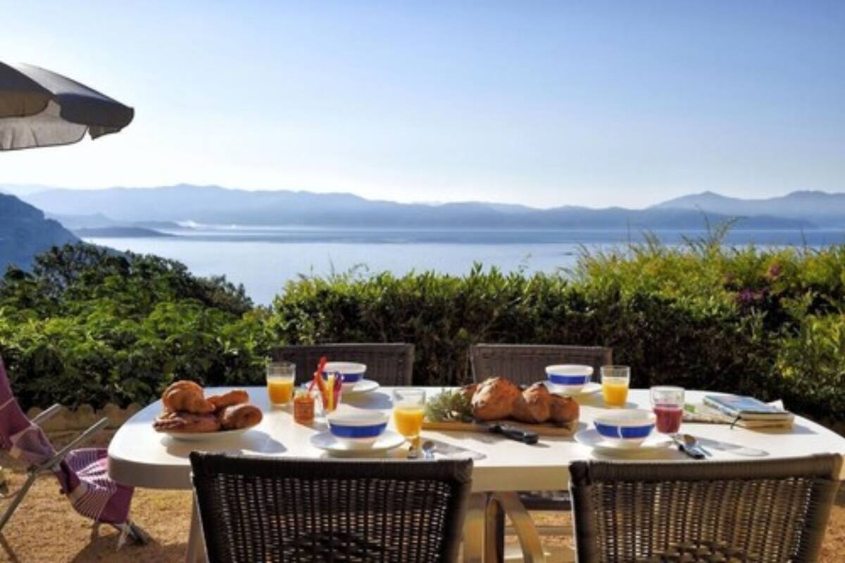 Una mesa de desayuno con croissants, zumo de naranja y una vista panorámica de montañas y un lago.