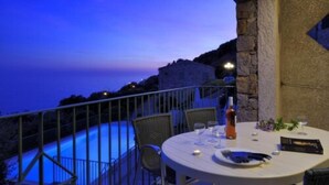 A dining table set for two with a view of a pool and a stone wall. - Résidence Roc e Mare (Cargese)