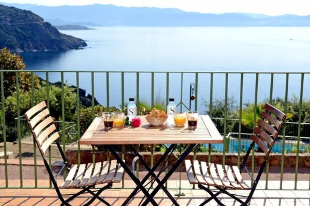 Una mesa con dos sillas, una botella de agua, una botella de jugo y una cesta de pan en una terraza con vista a un lago y montañas.