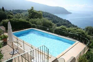 A rectangular swimming pool with a metal railing, surrounded by greenery and overlooking a coastal landscape. - Résidence Roc e Mare (Cargese)