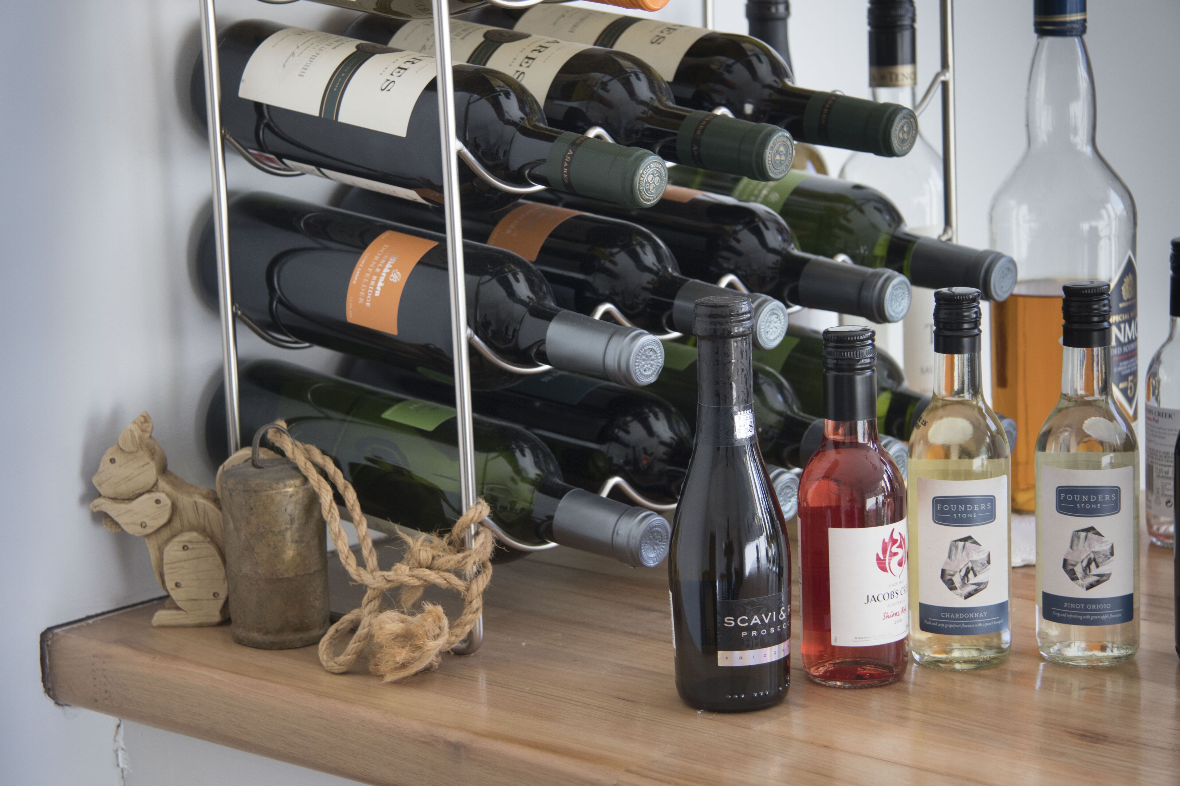 A wine rack with various bottles, a small wooden shelf with decorative items, and a few bottles on the table.