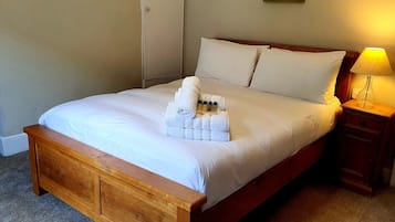 A neatly made bed with a wooden headboard, a bedside table with a lamp, and a stack of towels on the bed.
