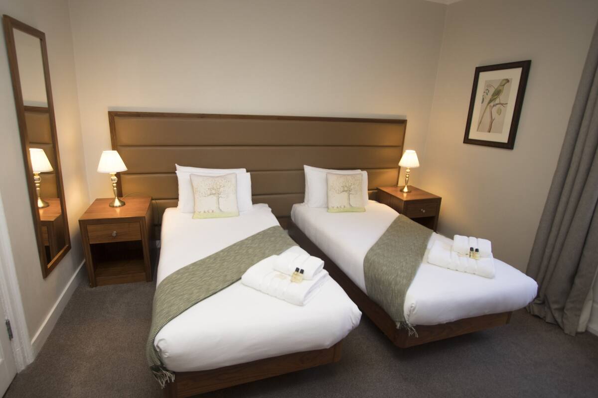 A hotel room with two beds, each with a pillow, a bedside lamp, and a towel.