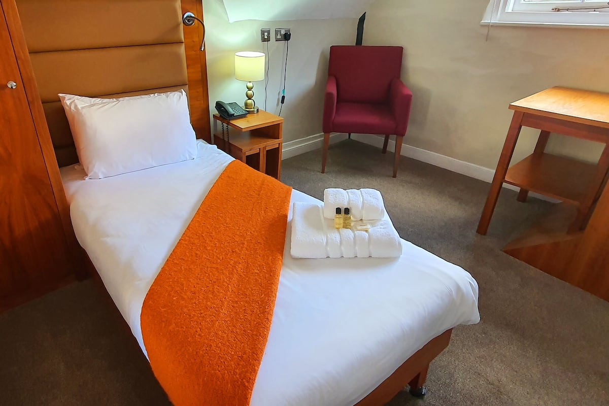 A hotel room with a bed, a chair, a desk, and a nightstand with a lamp and phone.