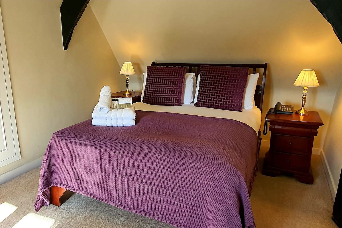 A bedroom with a large bed, two bedside tables with lamps, a wardrobe, and a carpeted floor.