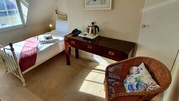 A small, tidy room with a single bed, a bedside table with a kettle, a chair, and a radiator.