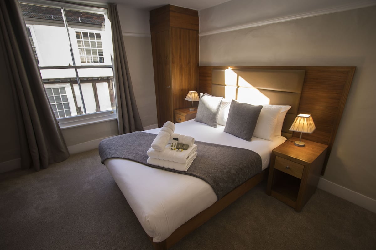 A neatly made bed with a headboard, two bedside tables with lamps, and a window with curtains.