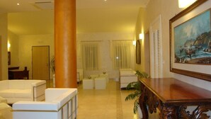 A spacious lobby with a large column, white sofas, a wooden reception desk, and a painting on the wall. - Il Galeone Bed and Breakfast (Taranto)