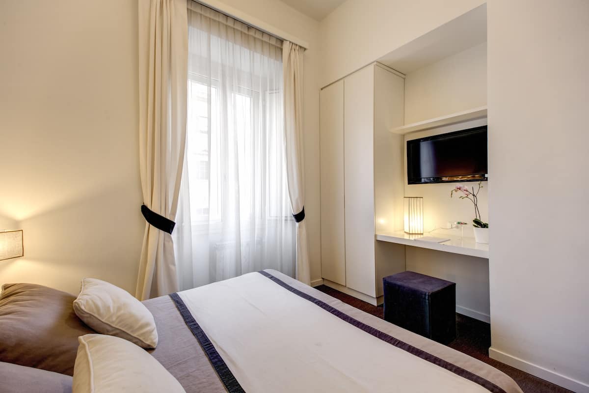 A hotel room with a bed, a desk, a television, and a window with curtains.