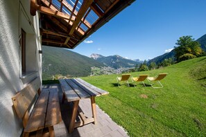 Una terraza de madera con mesa y sillas que da a un paisaje montañoso.