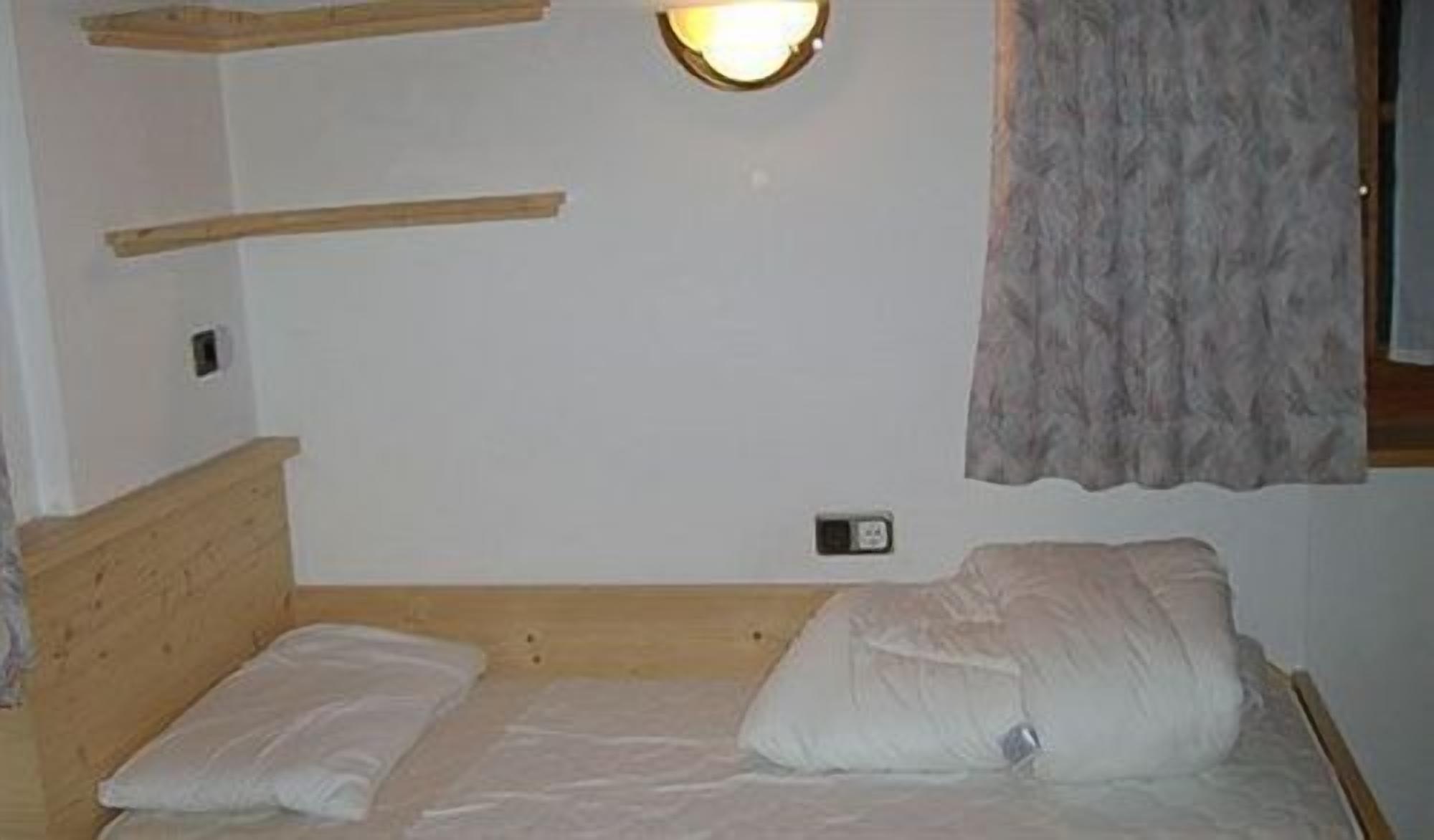Una camera da letto con una testiera in legno, un letto singolo con biancheria bianca, un lampadario a parete e una finestra con tenda.