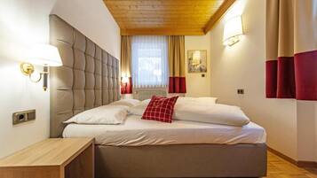 A bedroom with a large bed, a bedside table, a wall-mounted lamp, and a window with curtains.