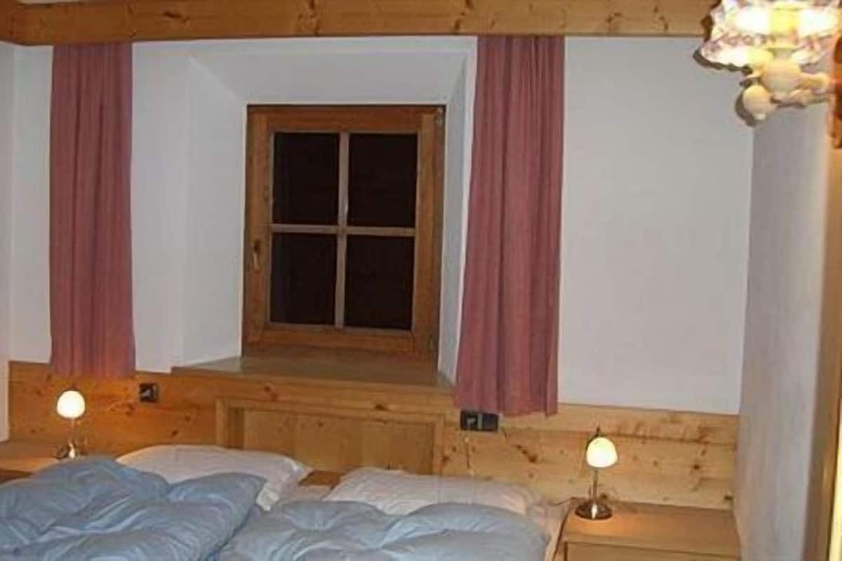 A cozy room with a wooden bed, two bedside lamps, and a window with curtains.