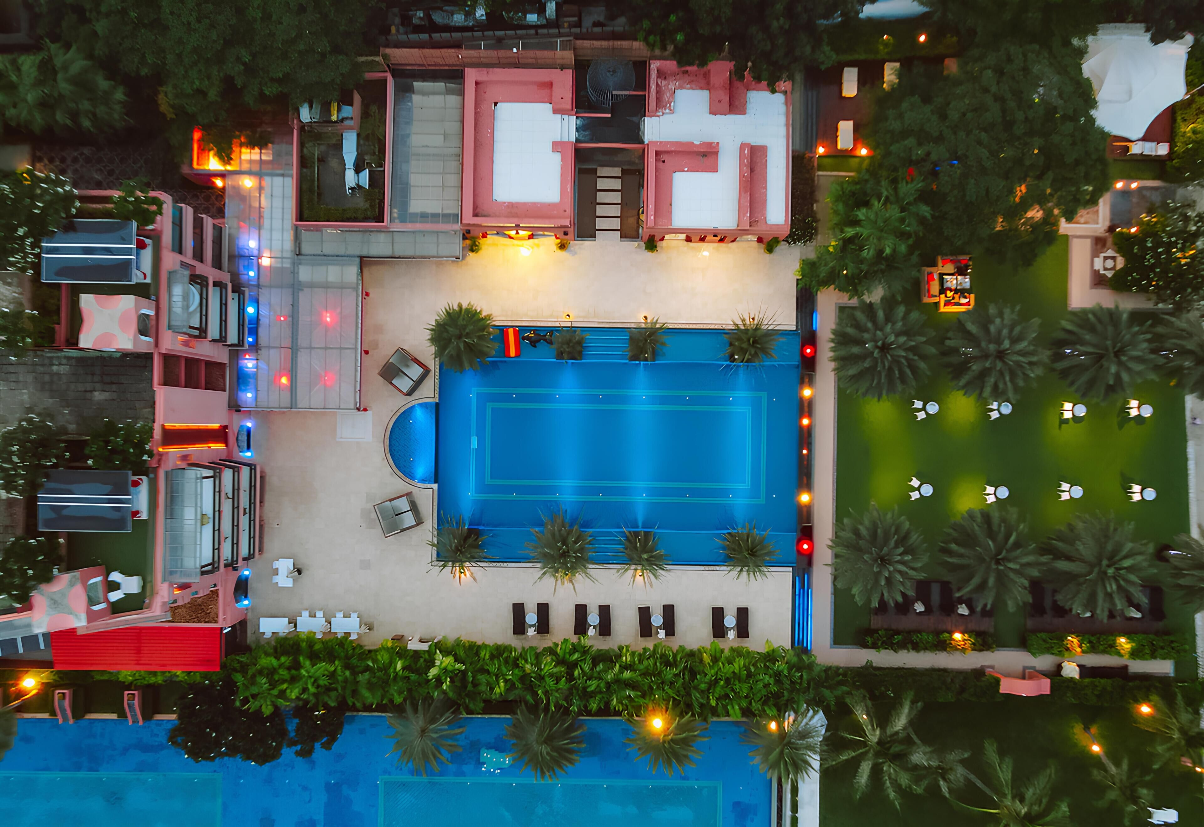 Vista aérea de un hotel con piscina, mobiliario exterior y un jardín cuidado.