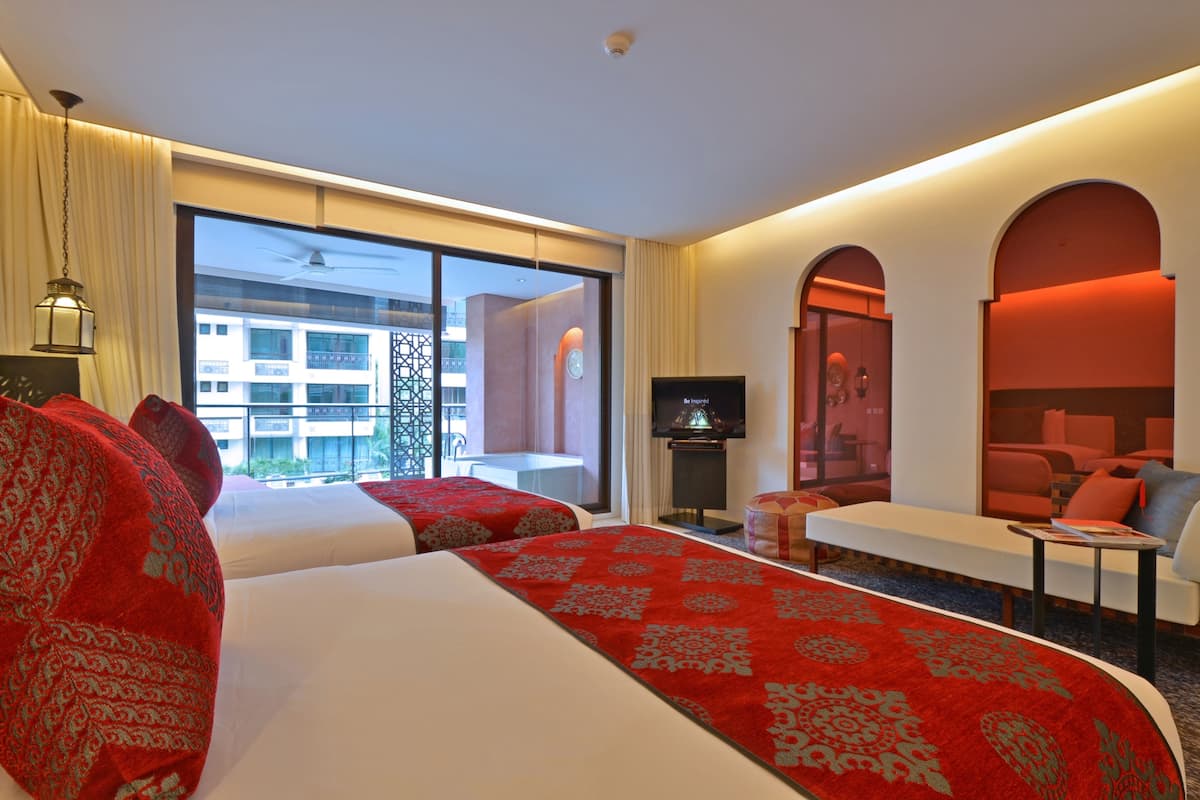 Une chambre d’hôtel avec deux lits, une télévision, un canapé et une grande fenêtre donnant sur des immeubles.