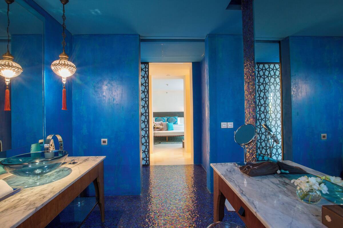 Une salle de bain moderne aux tons bleus, dotée d’un lavabo en verre en forme de bol et d’un comptoir en marbre.