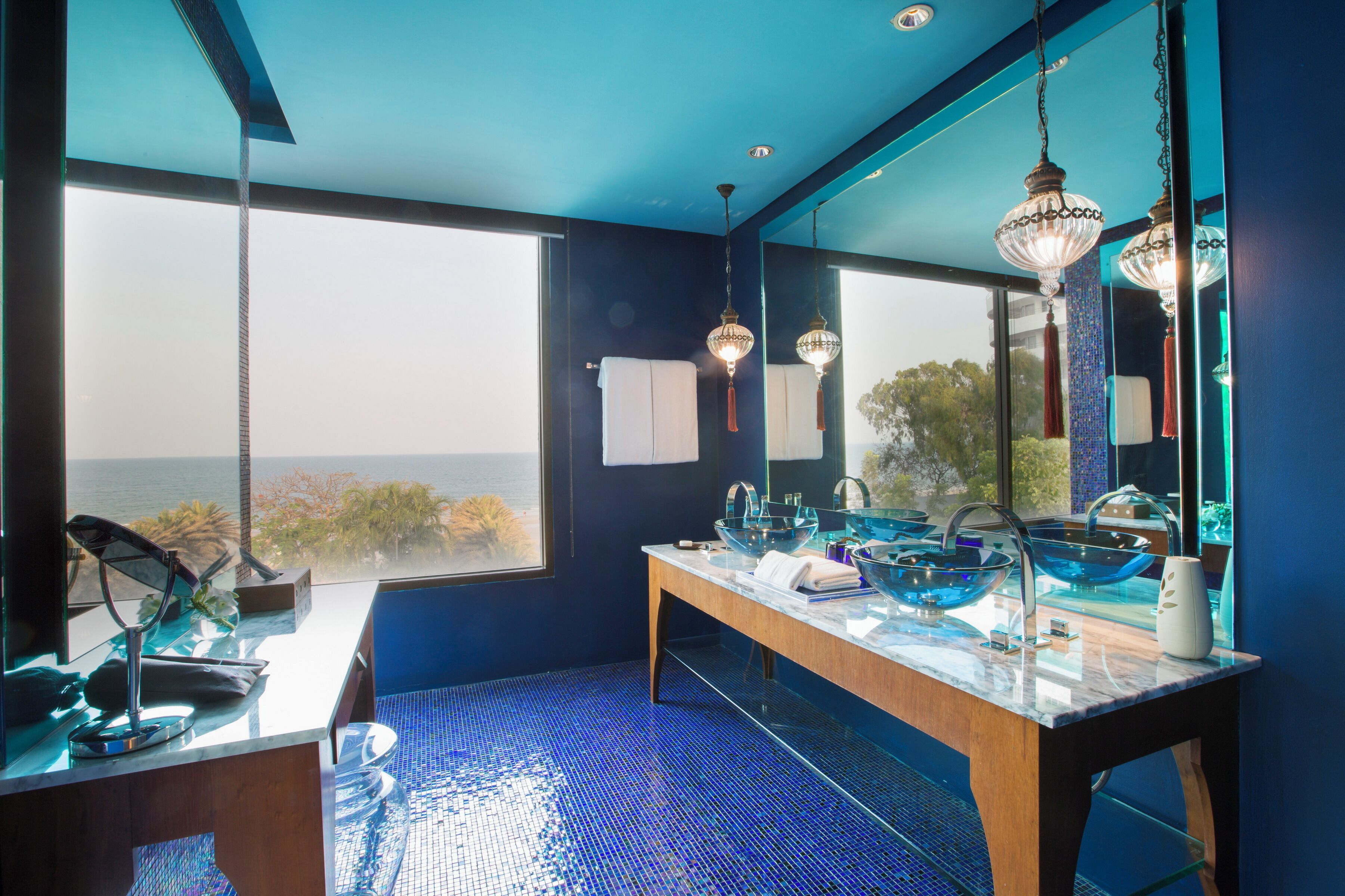 Un bagno moderno con un grande specchio, due luci a sospensione e vista mare.