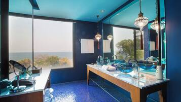 Un bagno moderno con un grande specchio, due luci a sospensione e vista mare.