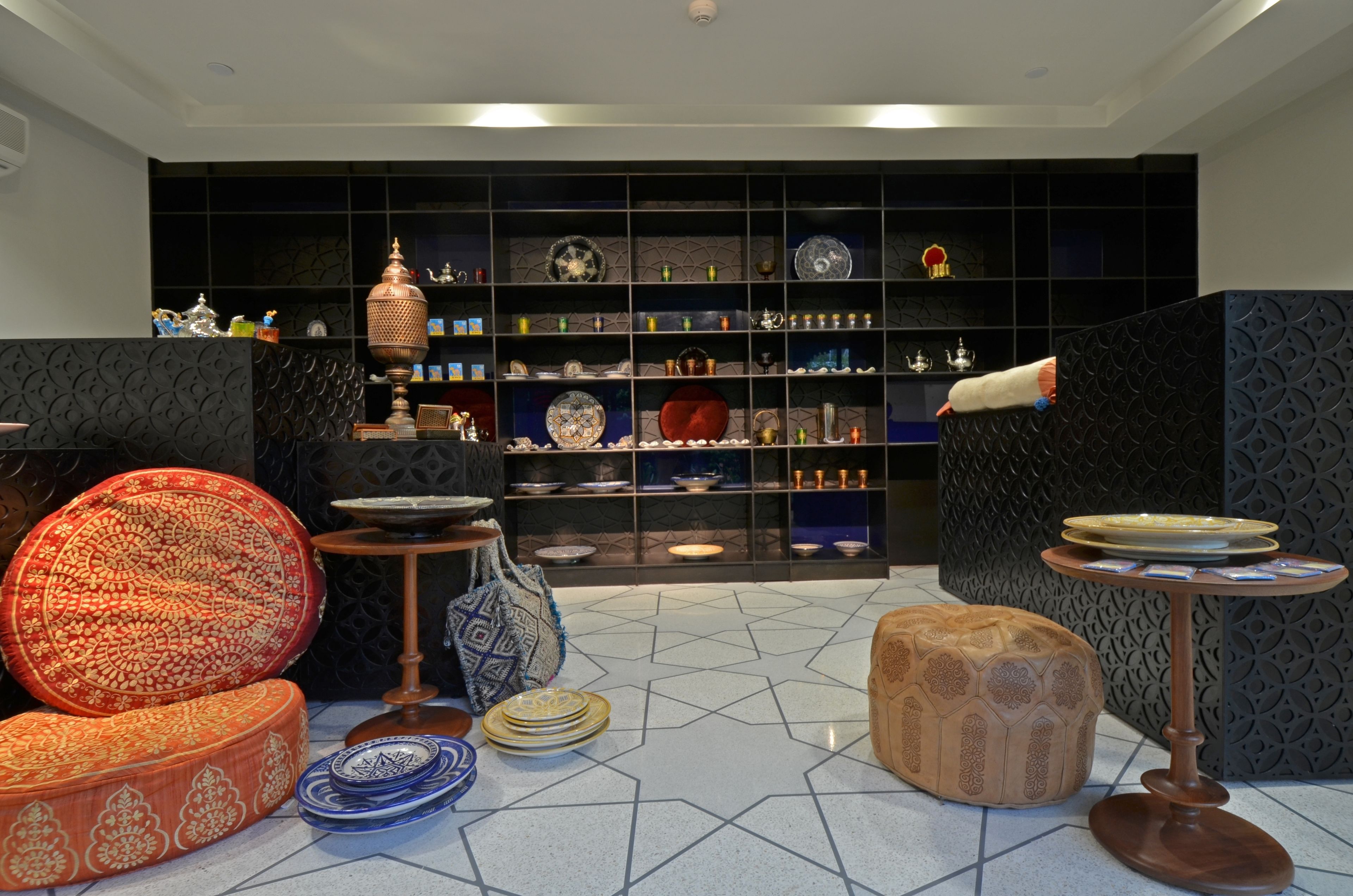 A room with a patterned floor, a sofa, a small table, and a shelving unit with various decorative items.