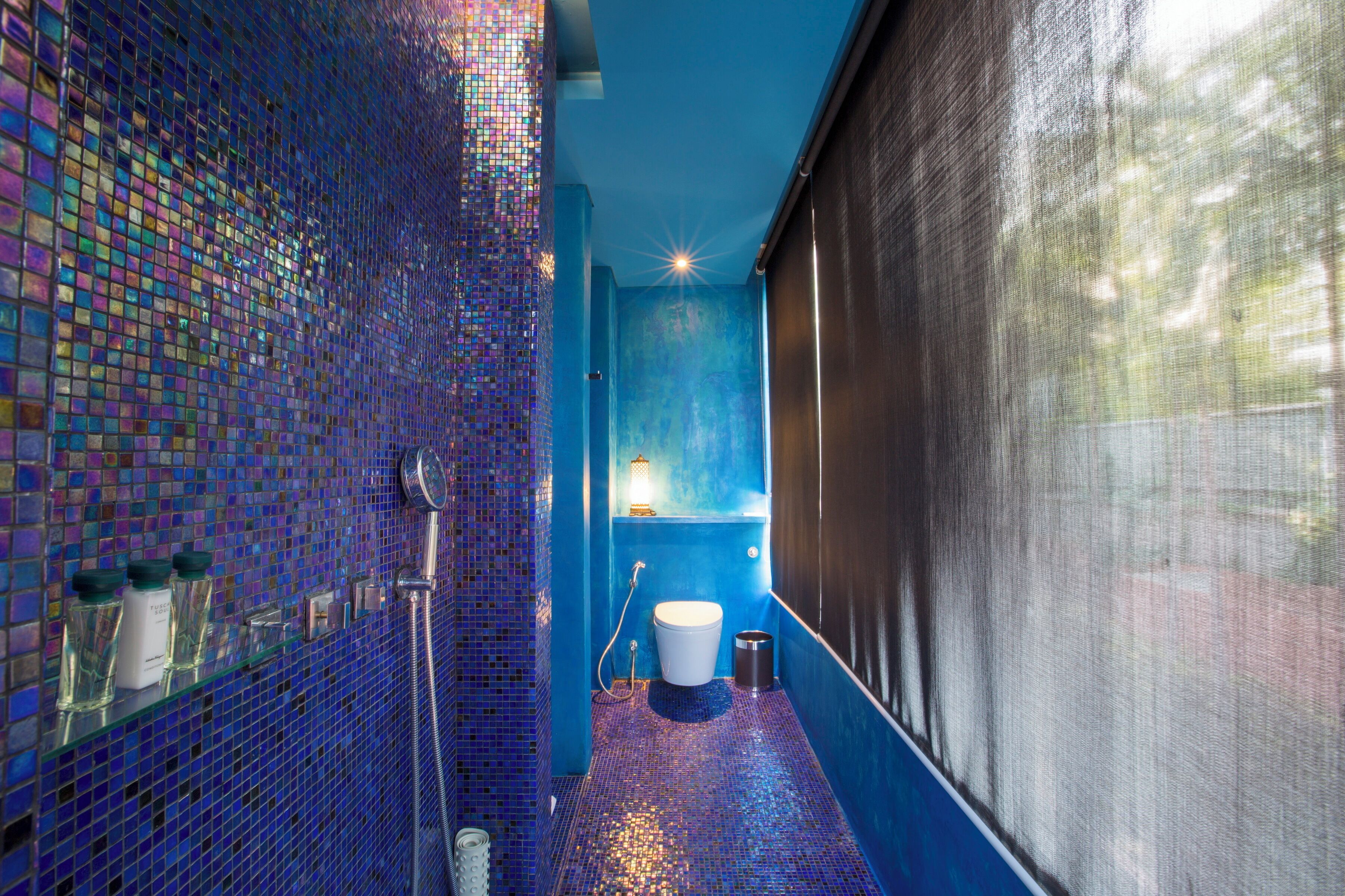 Un baño con pared de mosaico azul, inodoro blanco y zona de ducha.