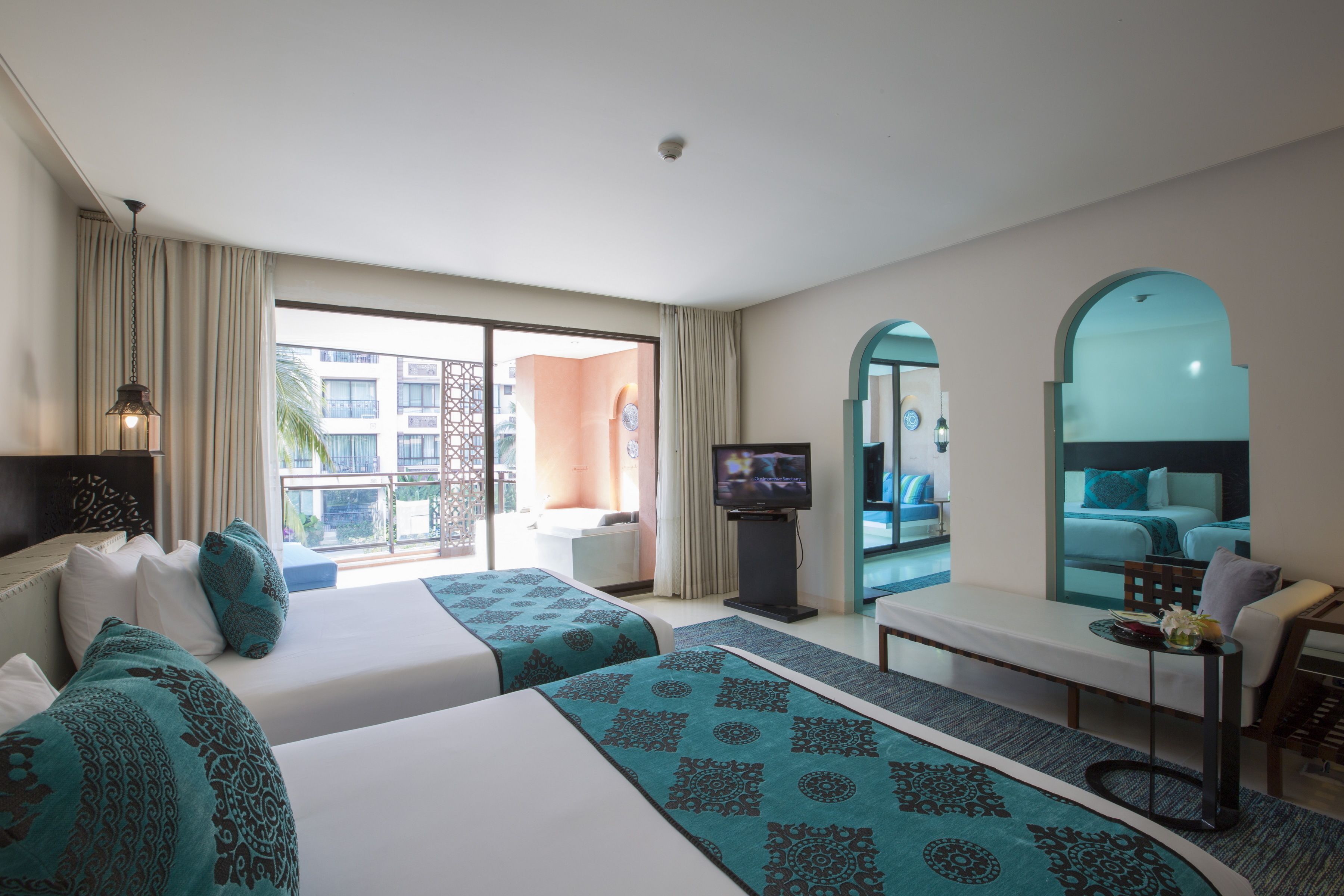 Une chambre d’hôtel avec deux lits, une télévision, un bureau et un balcon donnant sur les immeubles.