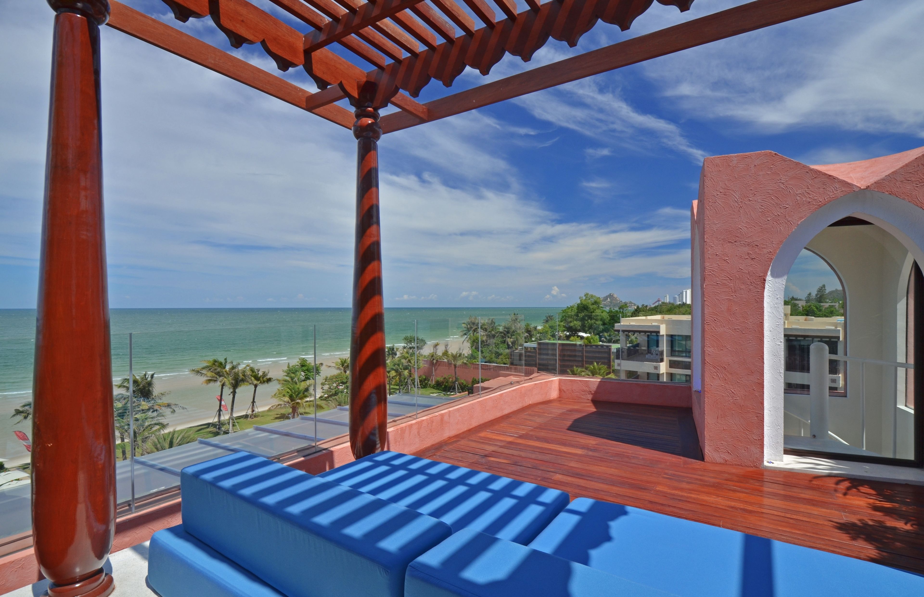 A wooden deck with blue cushioned seating, overlooking a beach and ocean.