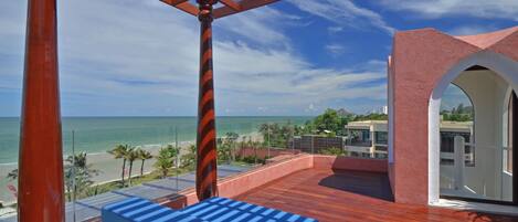 A wooden deck with blue cushioned seating, overlooking a beach and ocean.