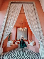 A room with a large window, a patterned wall, a chandelier, and a seating area with cushions.