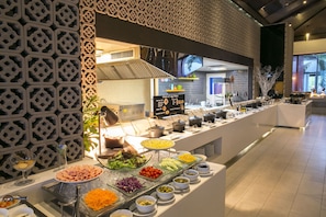 Un bufé con diversas opciones de comida, como ensaladas, carnes y quesos, dispuestas sobre una larga barra con paneles decorativos en la pared.