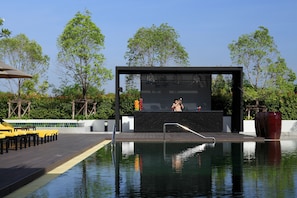 Un área de piscina moderna con un bar, sillones de descanso amarillos y una vista despejada del cielo.