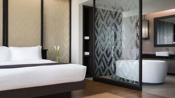 A modern hotel room with a large bed, a glass partition, a bathroom with a bathtub, and a mirror.