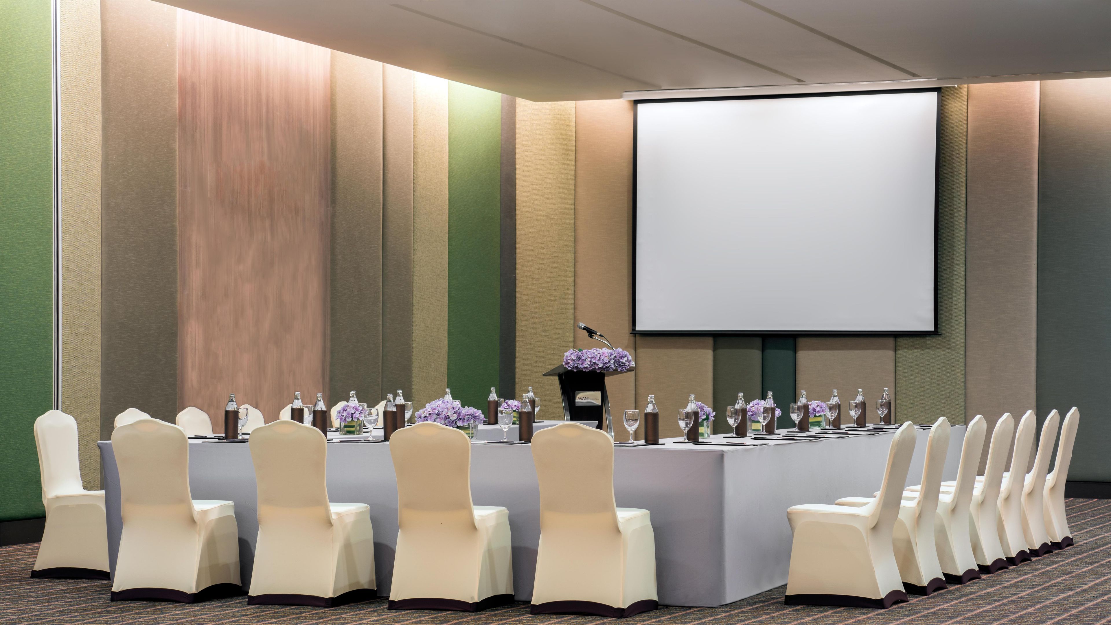 A conference room with a long table, chairs, a podium, and a projector screen.