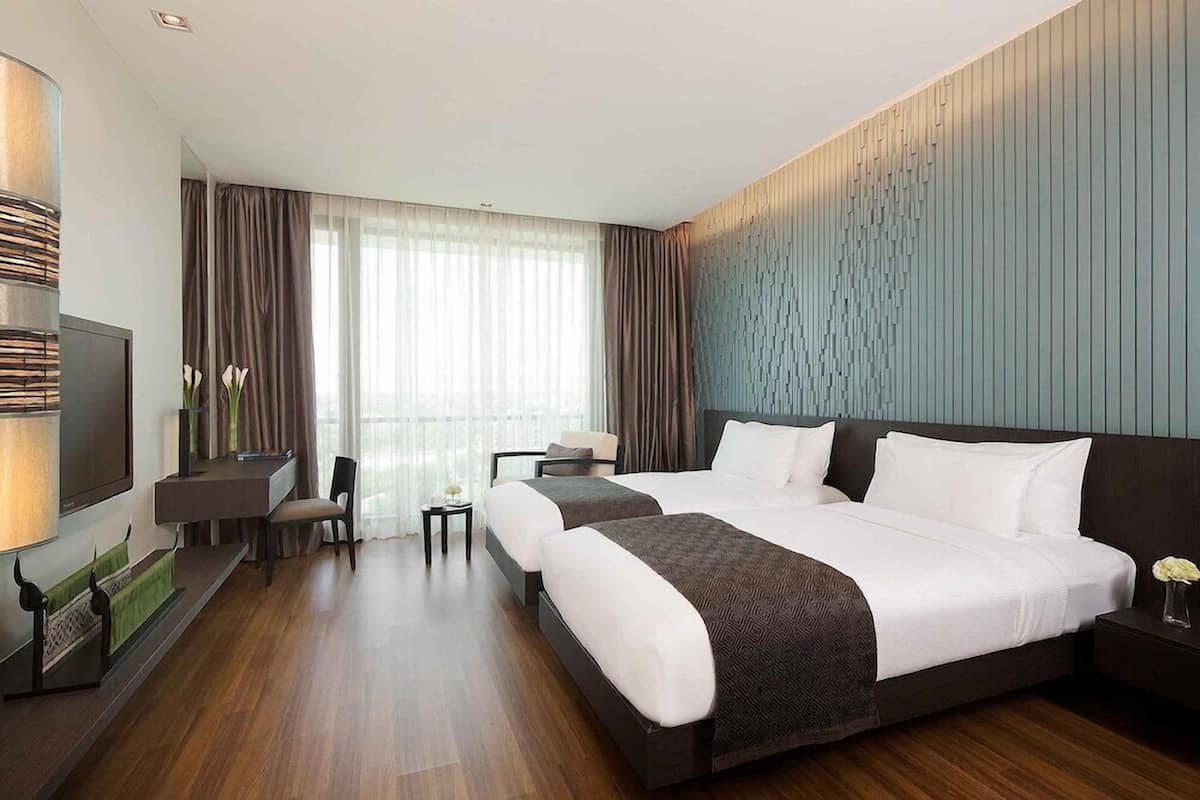A hotel room with a large bed, a desk, a chair, a TV, and a window with curtains.