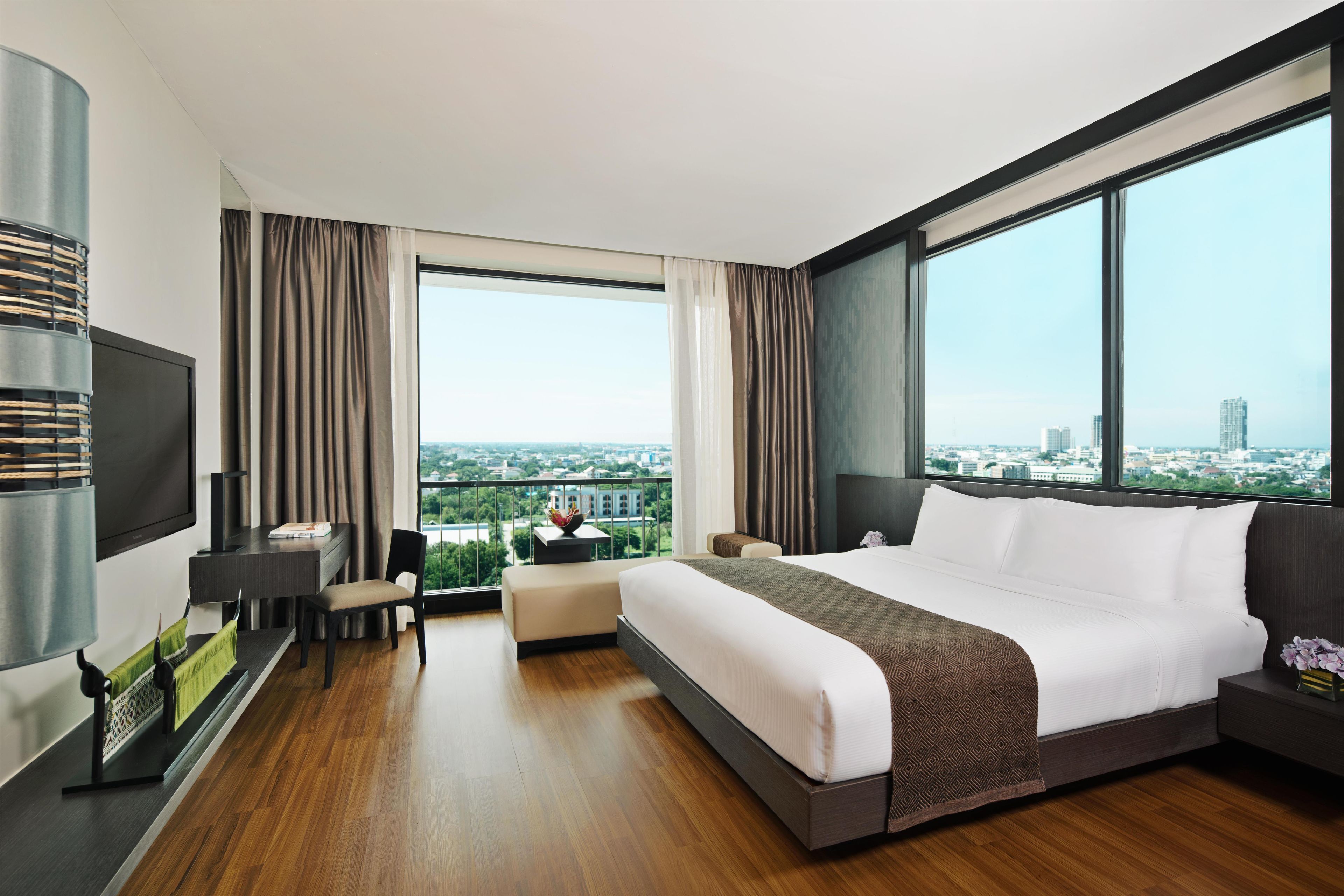 A modern hotel room with a large bed, a desk, a chair, and a TV.