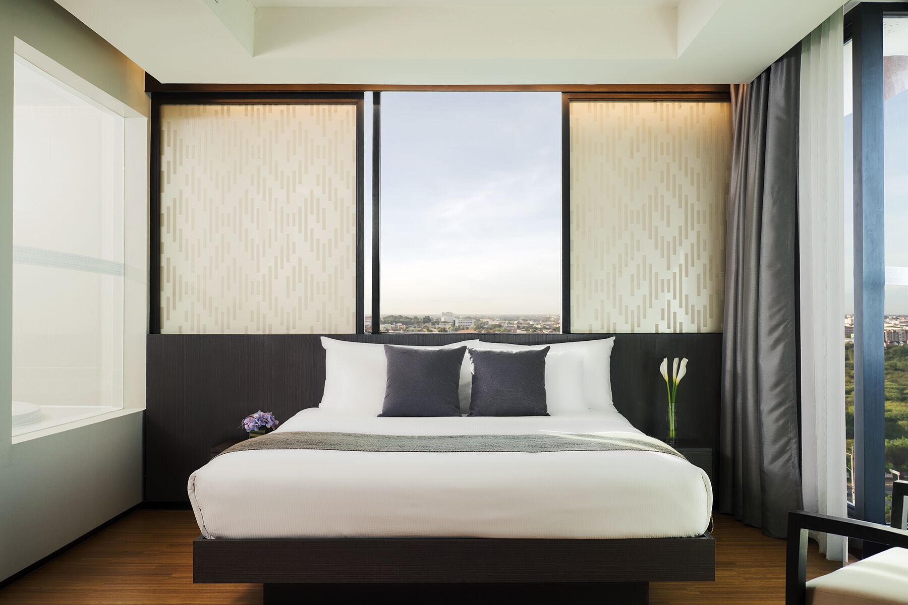 A modern hotel room with a large bed, a view of the city, and a window with curtains.
